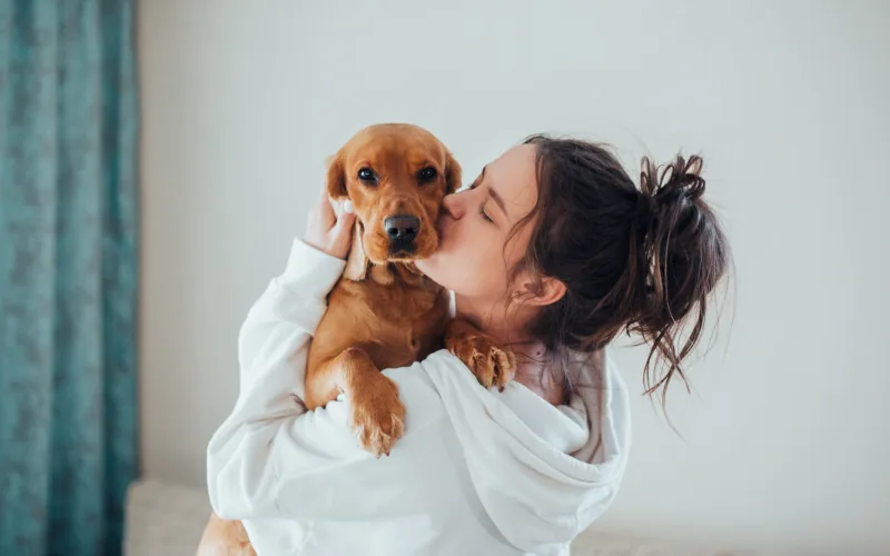 A woman hugging her dog close, eyes shut